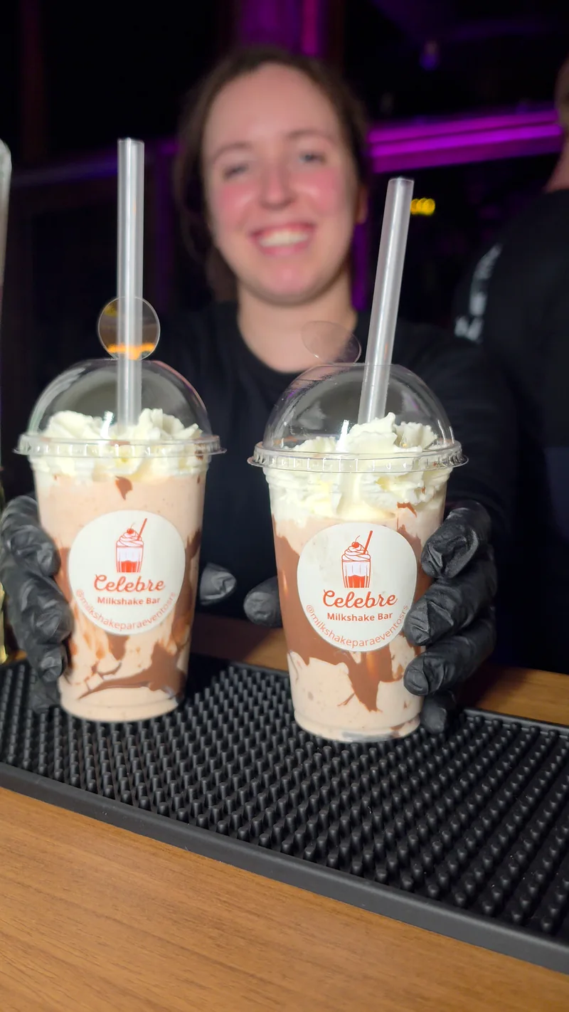 Integrante da equipe Celebre sorrindo e entregando dois milkshakes
